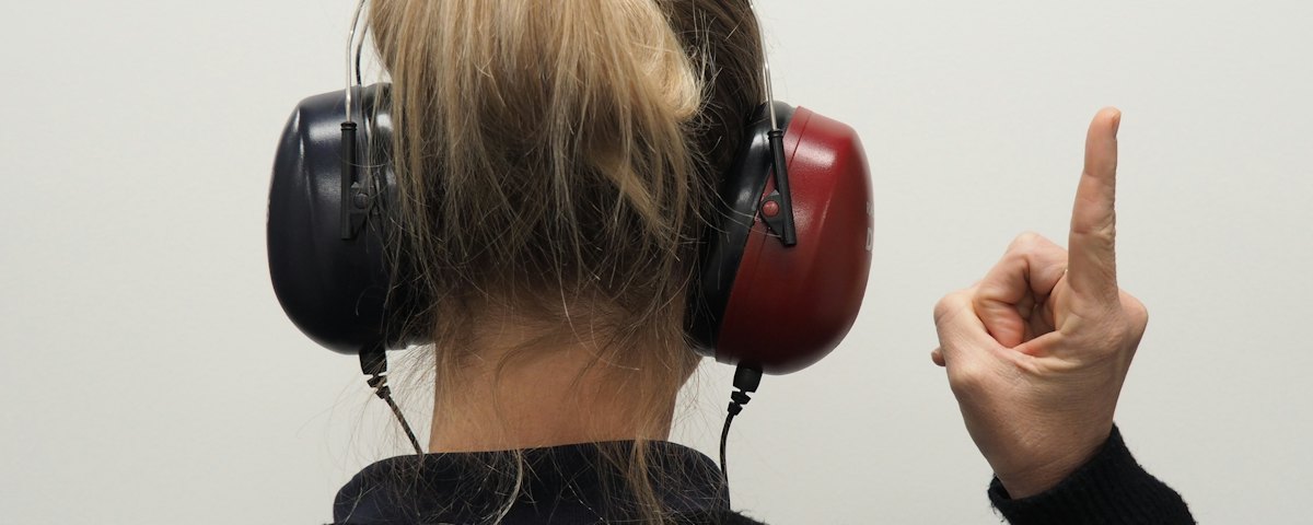 Person mit Kopfhörern hebt bei der Audiometrie den Finger, wenn sie den Ton hört
